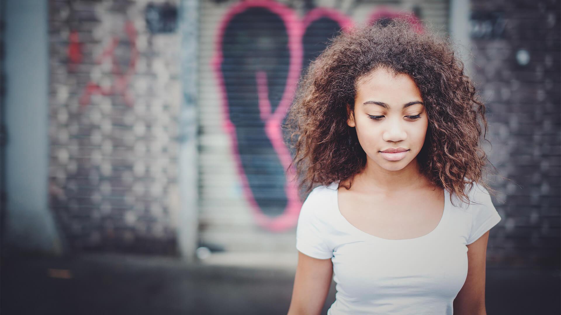Porträt einer jungen Frau mit Locken vor einer Graffiti-Wand